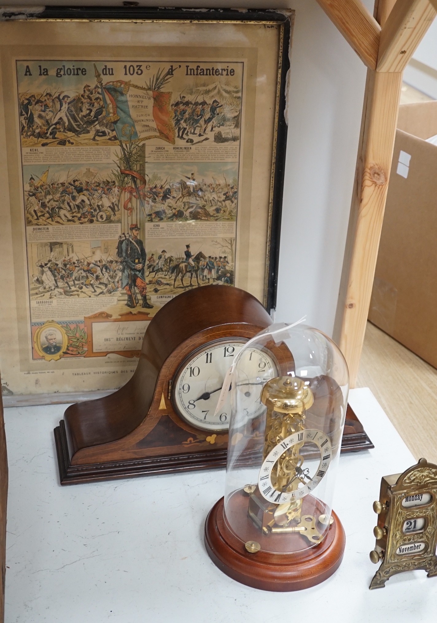 An early 20th century inlaid mahogany mantel clock, a skeleton clock under glass dome, a brass desk calendar and a 19th century French framed print, skeleton clock and dome 32cms high